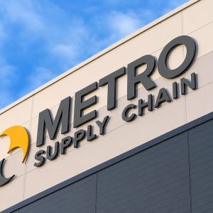 Storefront sign reading 'METRO SUPPLY CHAIN' with a yellow curved logo on a beige building against a blue sky, indicating a company sign.