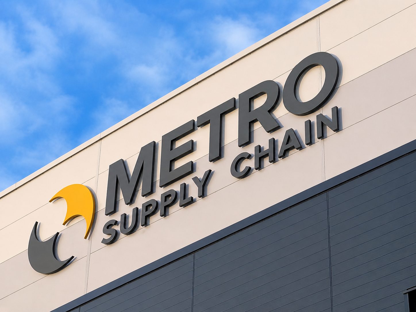 Storefront sign reading 'METRO SUPPLY CHAIN' with a yellow curved logo on a beige building against a blue sky, indicating a company sign.