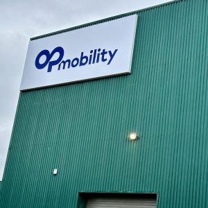 Green industrial building with a large white sign reading 'Op mobility' in blue, under a cloudy sky.