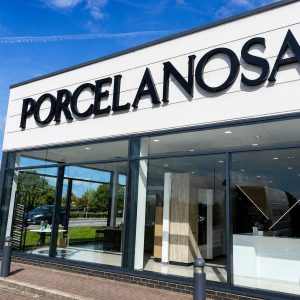 Storefront with large PORCELANOSA sign and glass showroom windows, blue sky above, interior displays visible inside