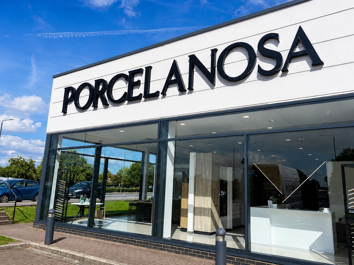 Storefront with large PORCELANOSA sign and glass showroom windows, blue sky above, interior displays visible inside