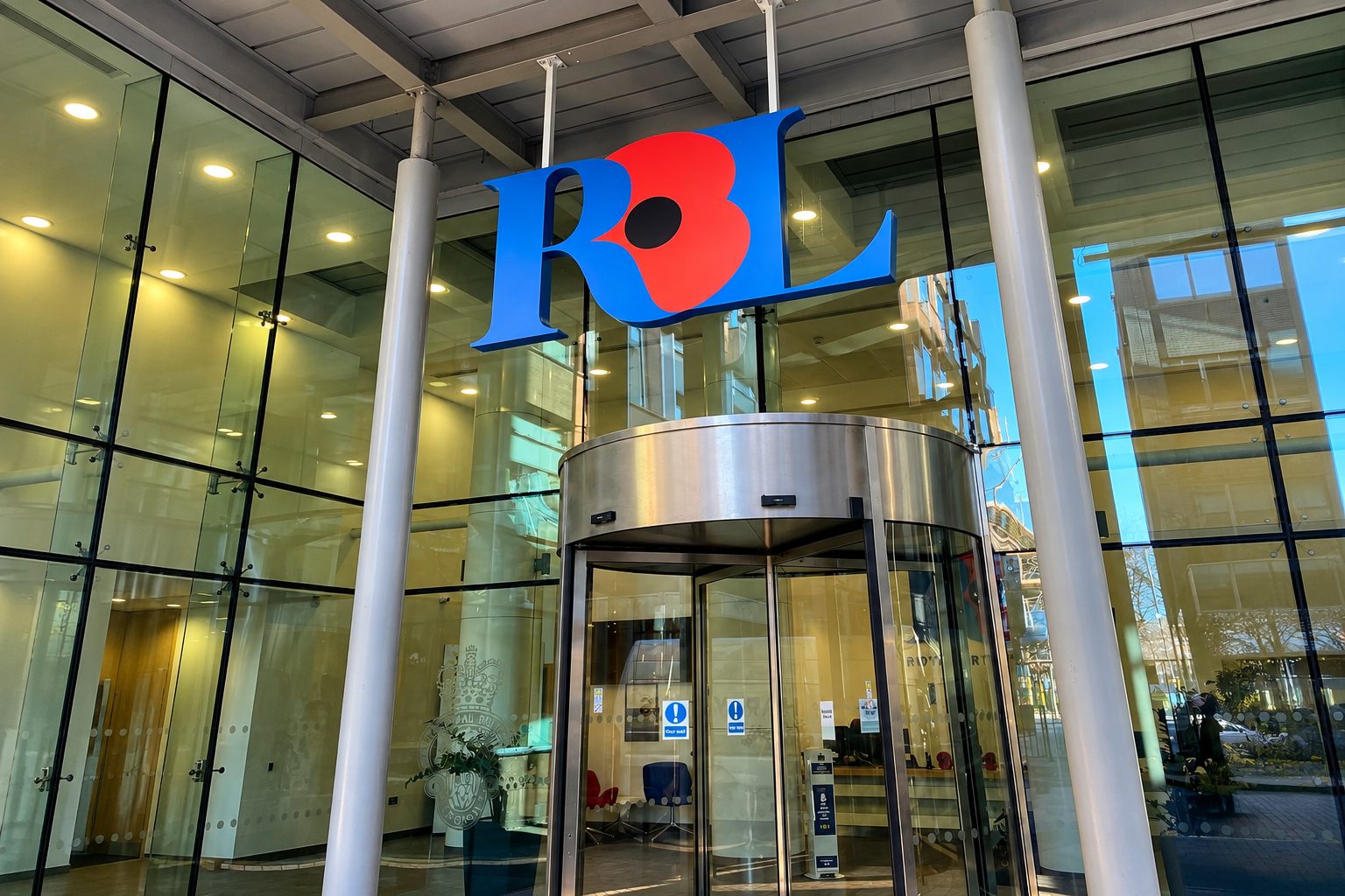 Exterior view of an RBL Bank entrance with a revolving door and glass storefront, large blue and red RBL logo above.