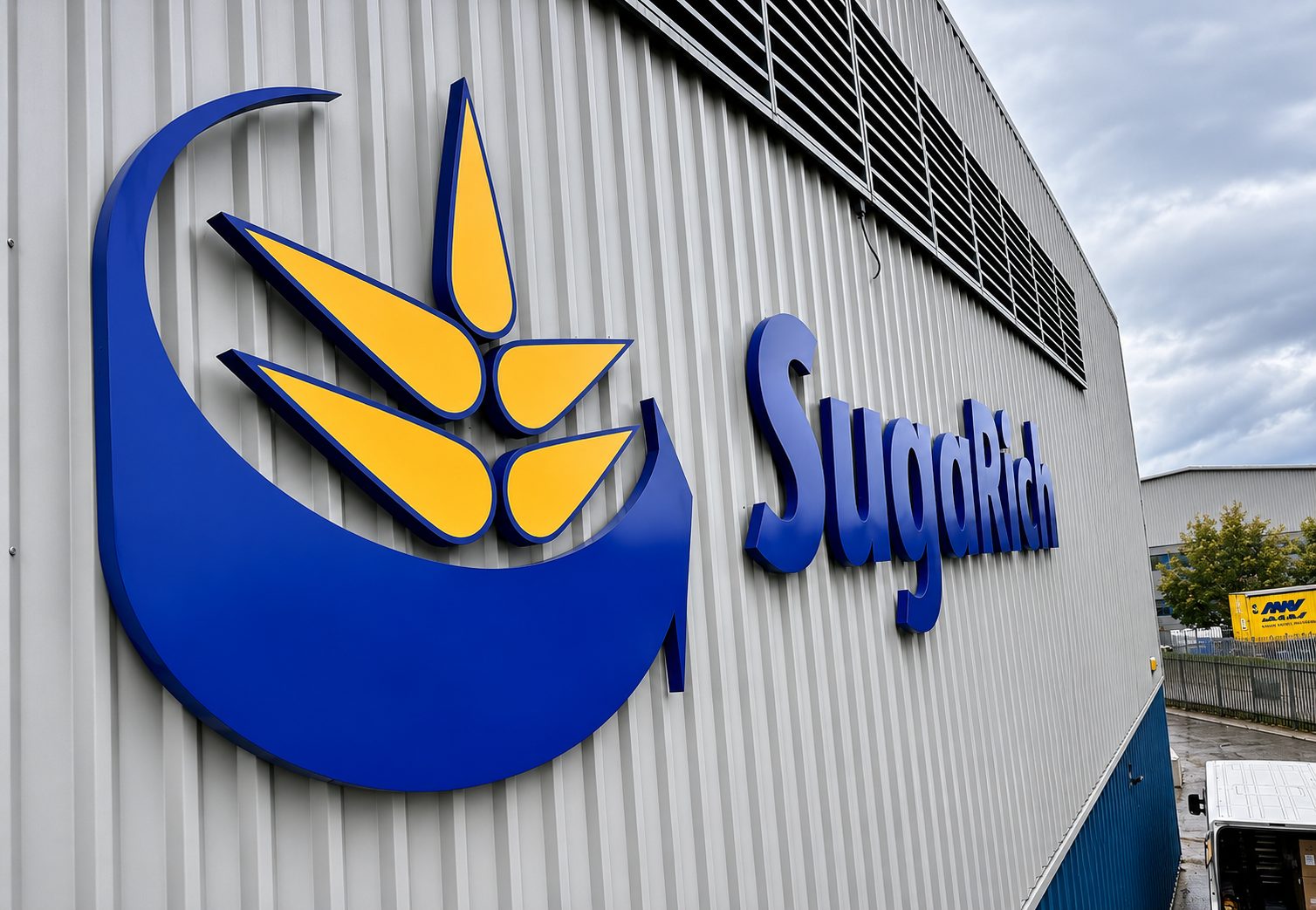 Exterior of a building with a large blue and yellow logo and the word 'SugRich' on corrugated metal siding.