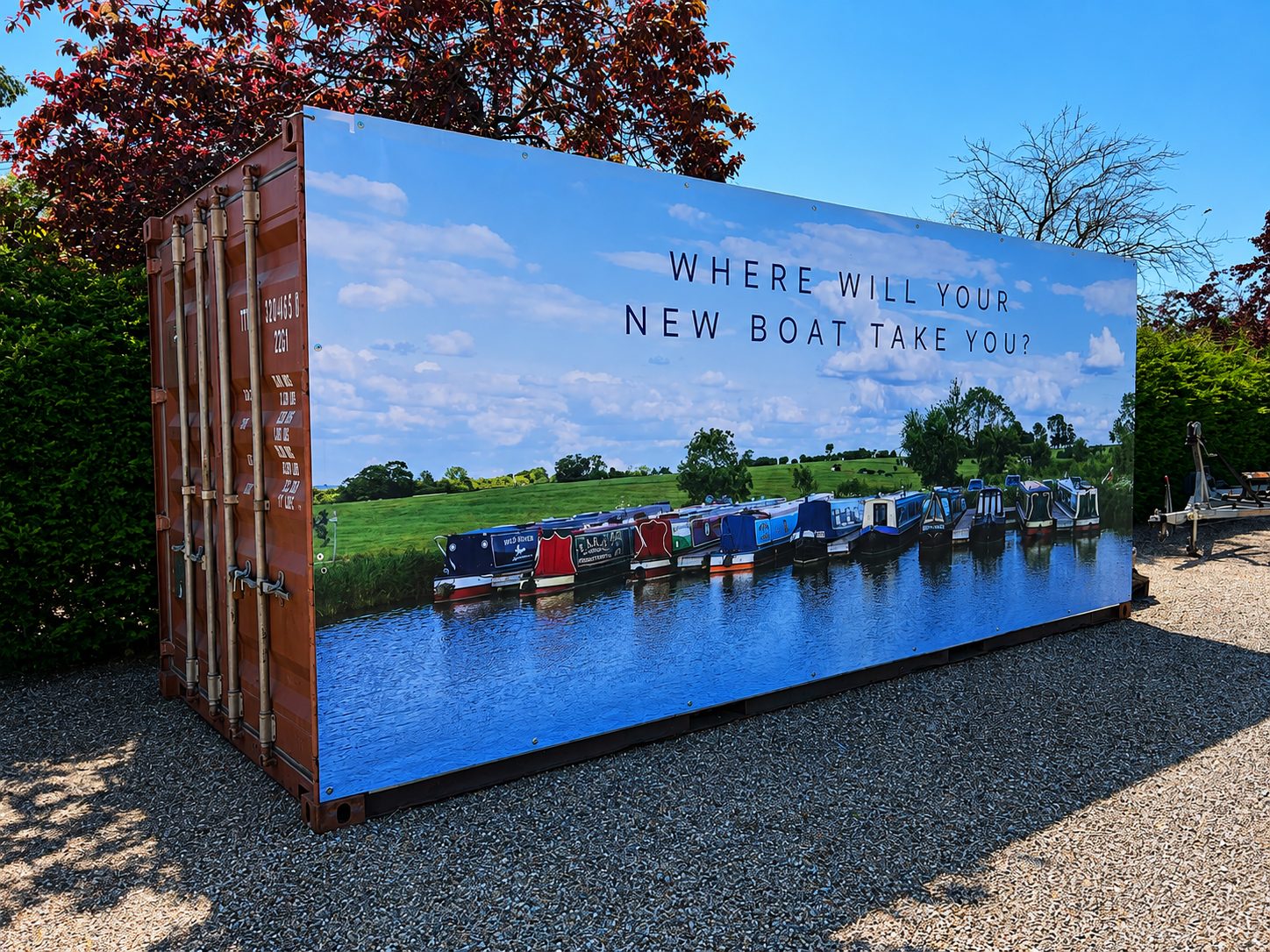Billboard on a shipping container showing a row of canal boats on a river with the caption 'Where will your new boat take you?'.