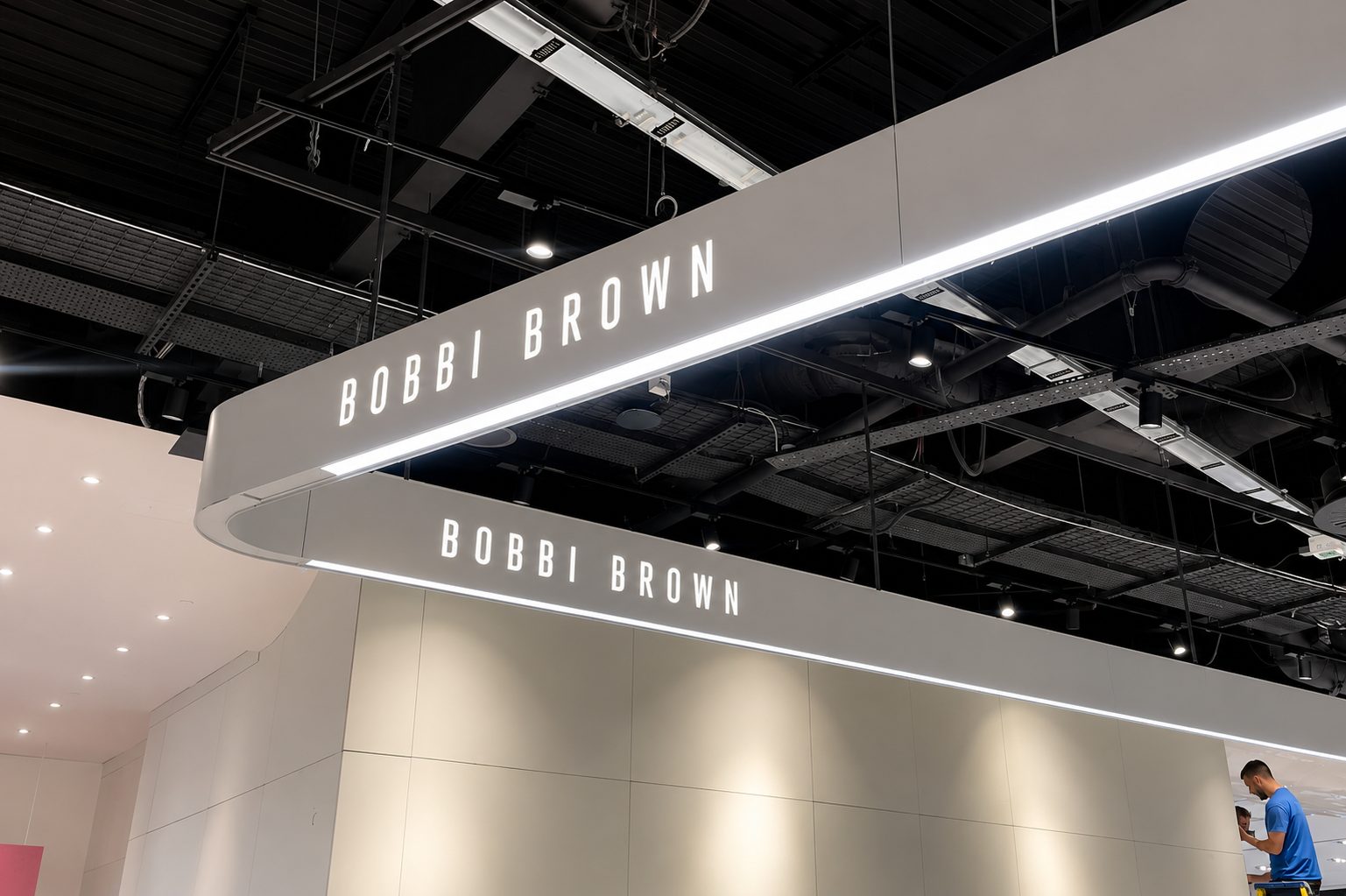 Overhead curved sign reading BOBBI BROWN in bright letters above a neutral retail booth.