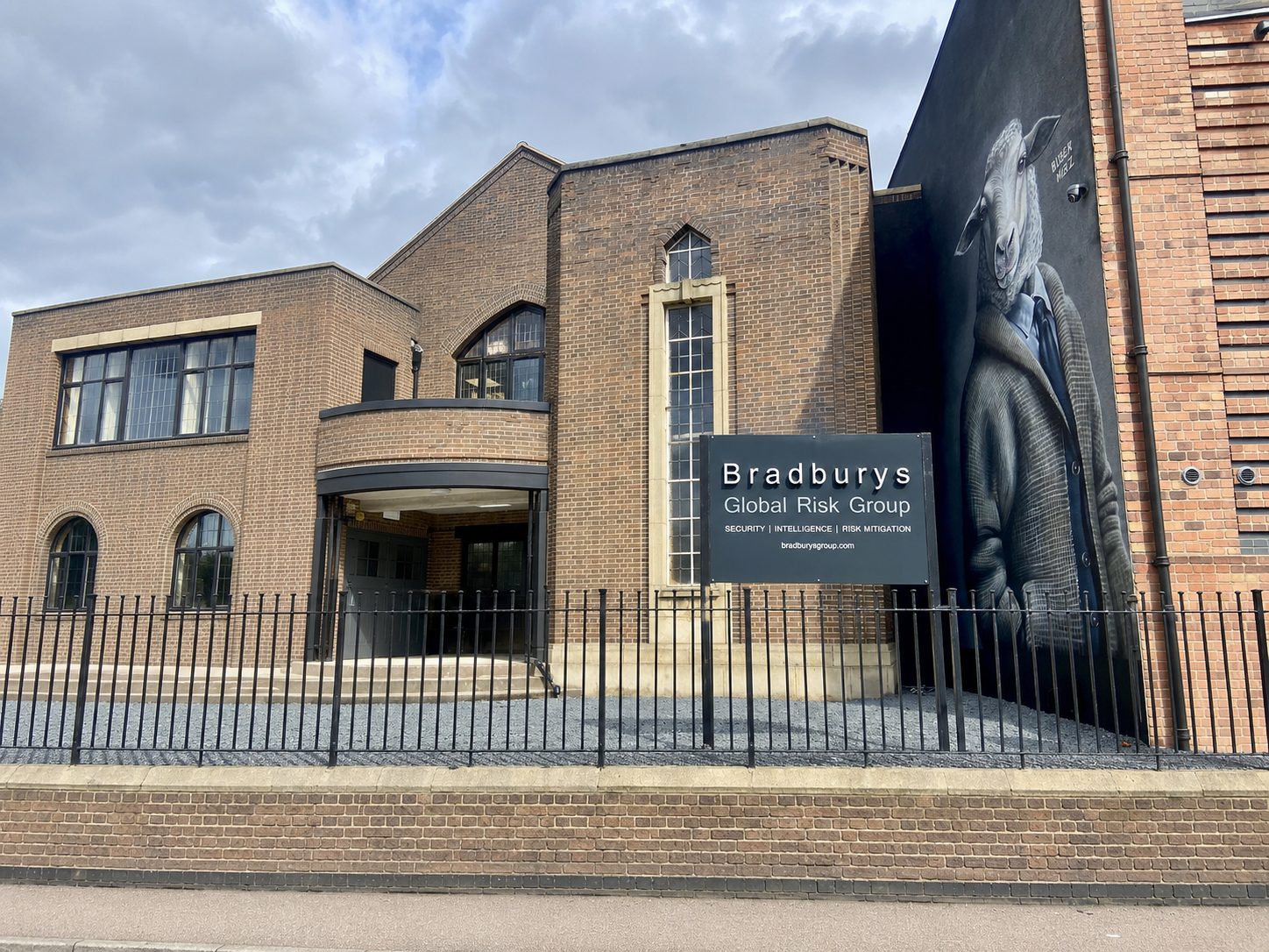 Brick office building with a Bradburys Global Risk Group sign near a tall narrow window and a large cow-mural on the right wall