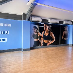 Gym studio wall with blue panels and motivational text; a photo of a fit woman running is displayed in the center on a wall mural.