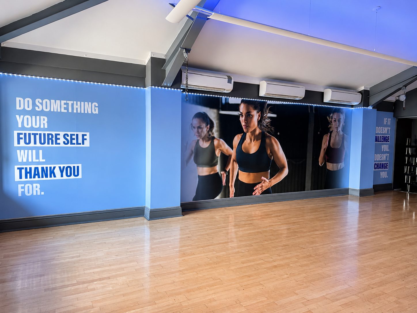 Gym studio wall with blue panels and motivational text; a photo of a fit woman running is displayed in the center on a wall mural.