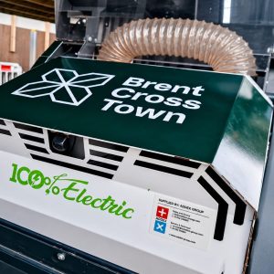 Industrial machine in a workshop with Brent Cross Town branding and a 100% Electric logo visible on the unit.