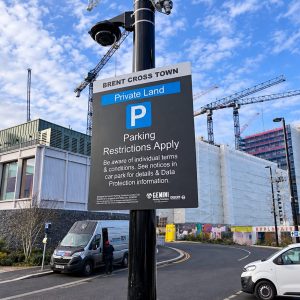 Large sign on a lamppost announcing private land parking restrictions near a construction site with cranes in the background, Brent Cross Town.