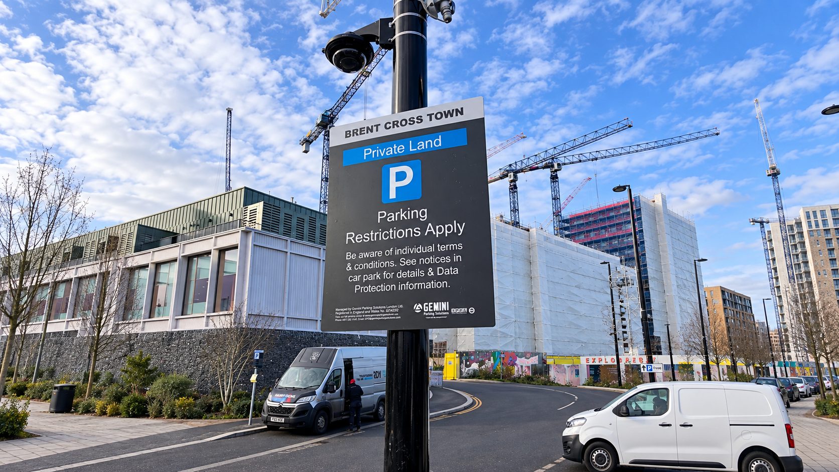 Large sign on a lamppost announcing private land parking restrictions near a construction site with cranes in the background, Brent Cross Town.