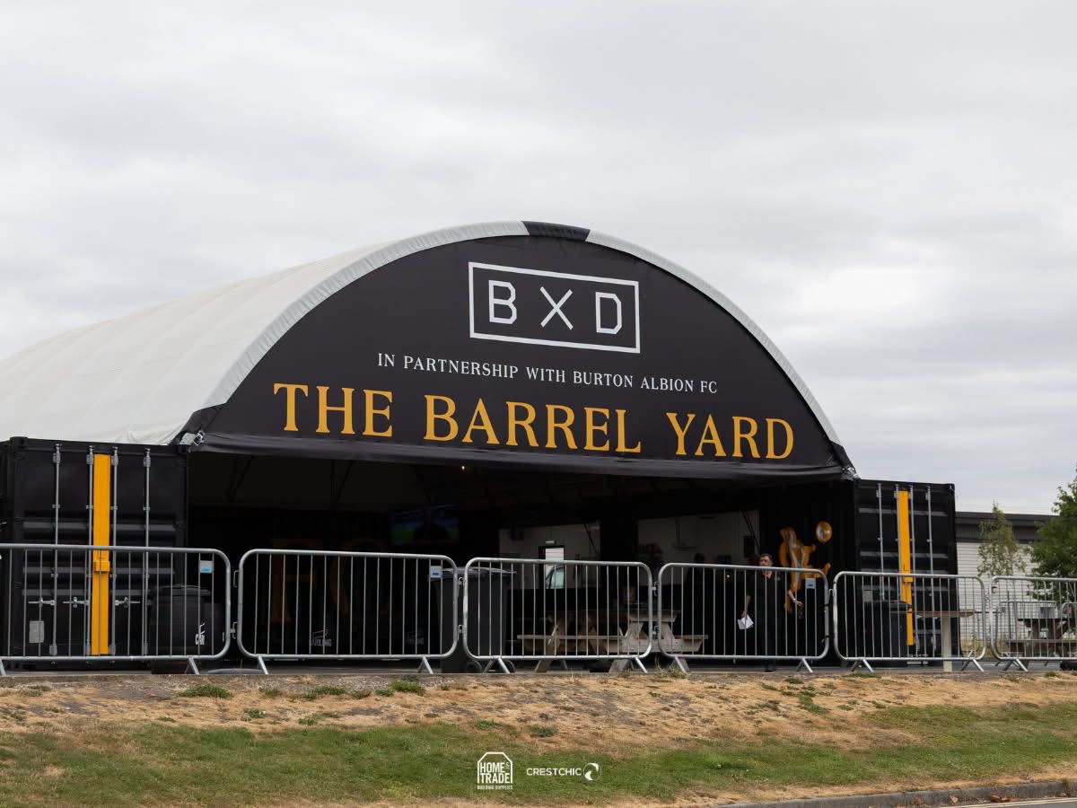 Black outdoor event tent labeled THE BARREL YARD with the BXD logo, metal barriers in front, under a cloudy sky.