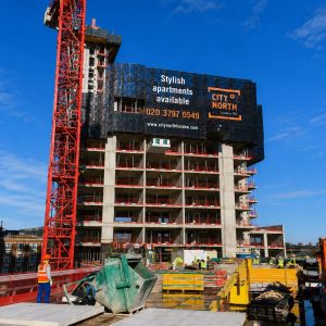 Under-construction high-rise with a red crane and a billboard advertising stylish apartments by City North London on a bright day.