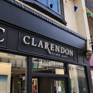 Black storefront signage reading 'CLARENDON FINE ART' with large 'C' logo and gallery windows reflecting street life