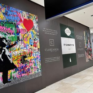 Large colorful graffiti mural on a gallery wall with a black silhouette reaching up, in a museum-like corridor.