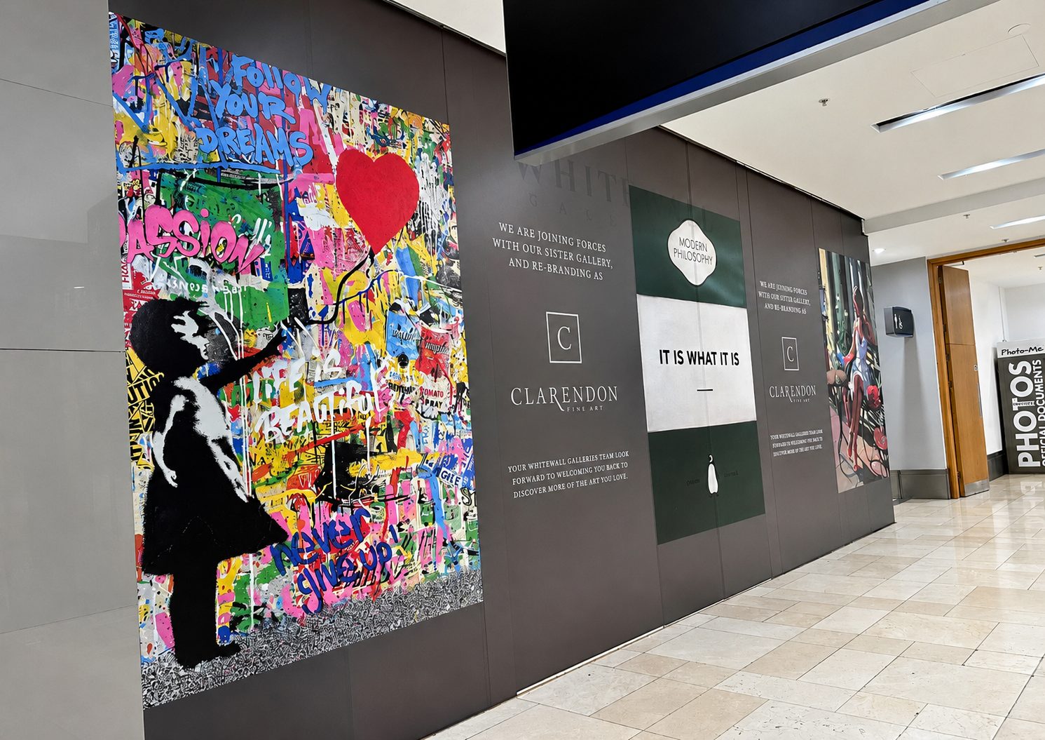 Large colorful graffiti mural on a gallery wall with a black silhouette reaching up, in a museum-like corridor.
