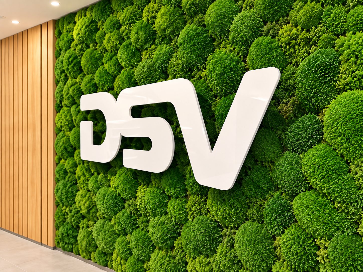 White glossy three-dimensional letters 'BSV' mounted on a green moss wall with wooden slat paneling on the left in a modern interior.