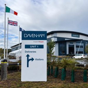 DAVENHAM building with a large UNIT 1 sign showing directions for Deliveries and Visitors; flags fly in front.