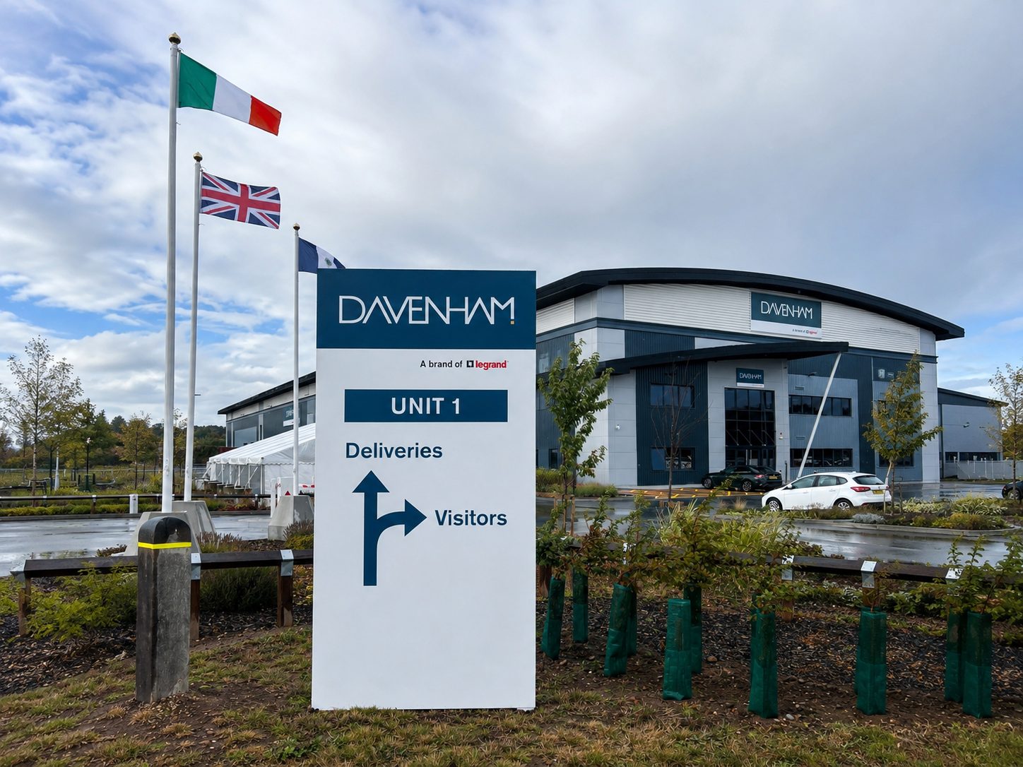 DAVENHAM building with a large UNIT 1 sign showing directions for Deliveries and Visitors; flags fly in front.