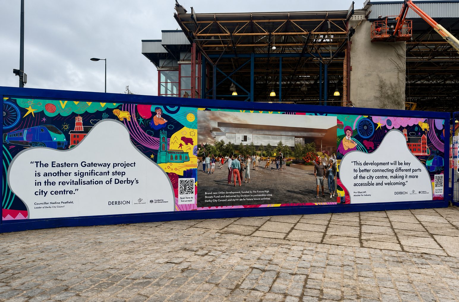 Colorful bannered construction fence with quotes about Derby's city centre and a photo of people in a plaza near a modern building under construction.