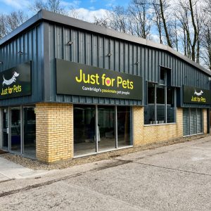 Exterior view of a pet store called Just for Pets, with black signs and yellow lettering on a blue metal building.