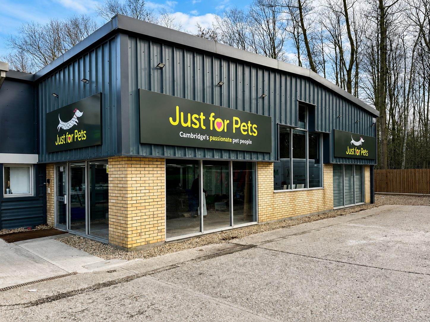 Exterior view of a pet store called Just for Pets, with black signs and yellow lettering on a blue metal building.