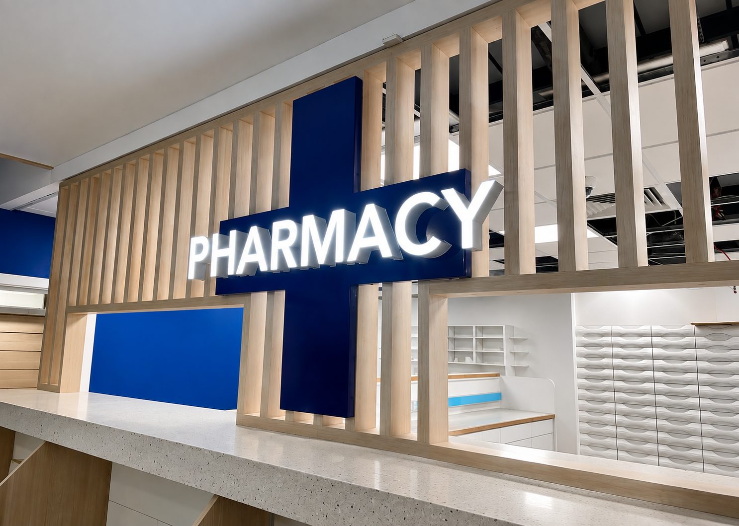 Modern pharmacy counter with a bright white 'PHARMACY' sign mounted on a blue cross, behind a light wood slat divider.