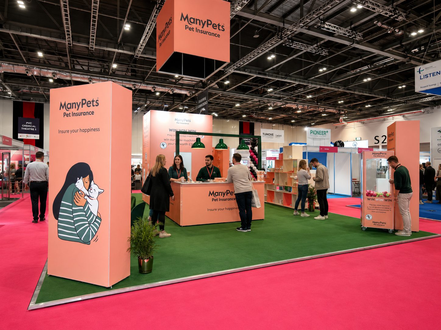 Exhibition booth for ManyPets Pet Insurance with pink panels, a green carpet, and staff at a reception desk.