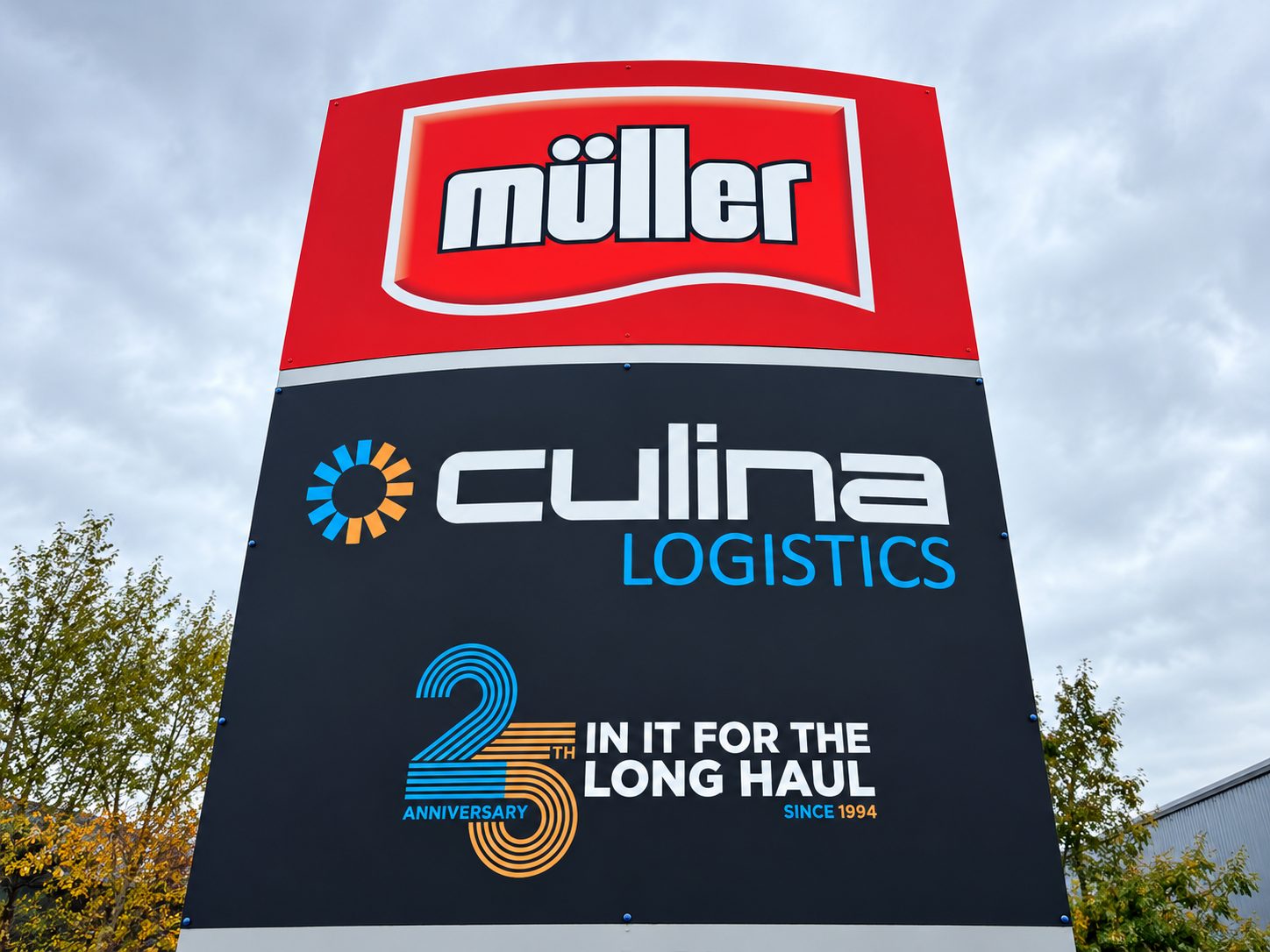 Outdoor sign featuring Müller logo above Culina Logistics branding, with a blue‑orange 25th anniversary graphic and the text 'In it for the long haul'.