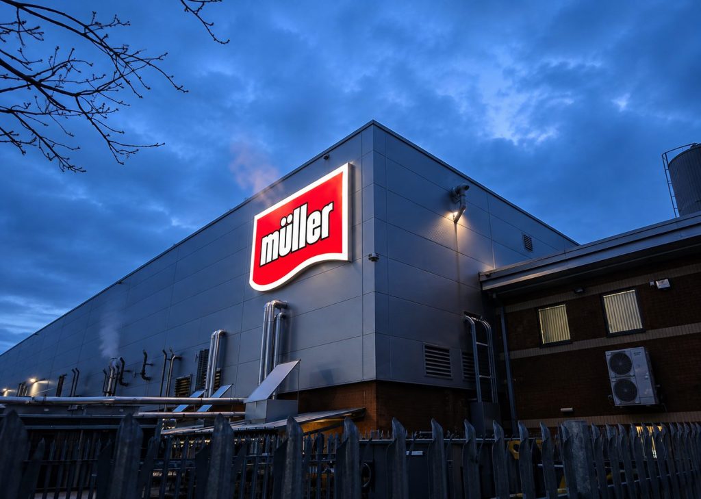 Industrial building at dusk with illuminated Miller logo on the side wall.