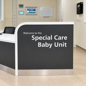 Reception desk in a hospital neonatal unit with a curved front reading 'Welcome to the Special Care Baby Unit'