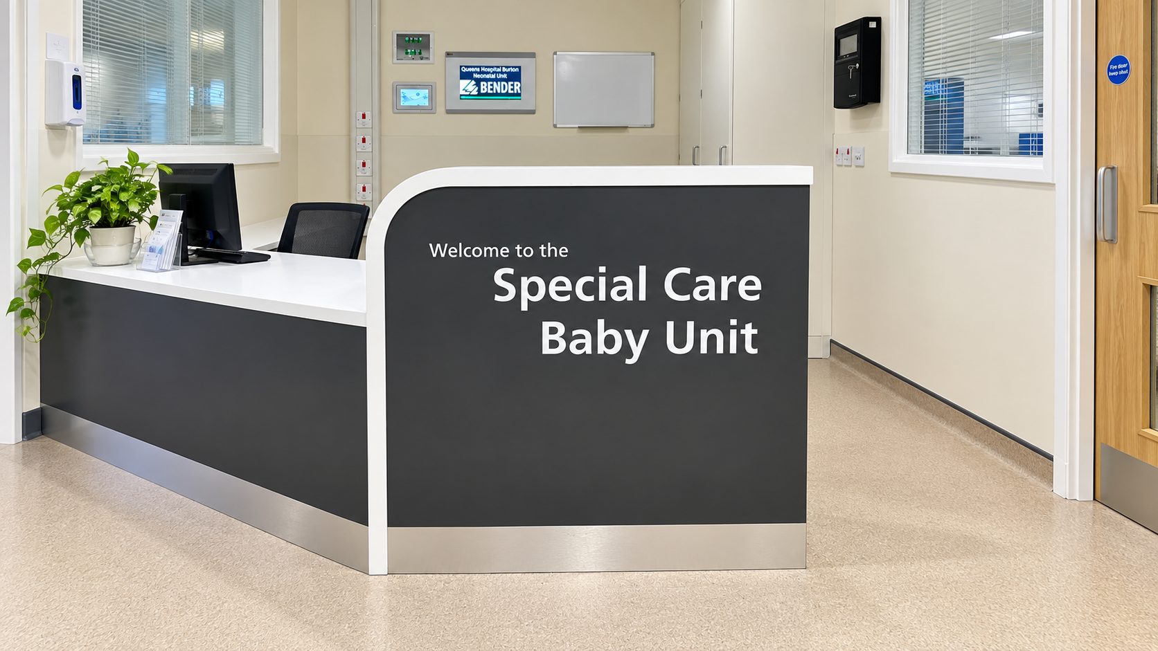Reception desk in a hospital neonatal unit with a curved front reading 'Welcome to the Special Care Baby Unit'