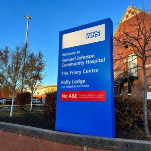 Blue NHS sign outside Samuel Johnson Community Hospital listing The Friary Centre and Holly Lodge with 'No A&E' notice (informational)