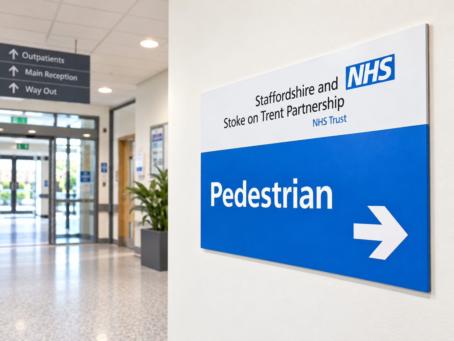 NHS pedestrian sign on a white wall showing an arrow to the right in a hospital corridor.