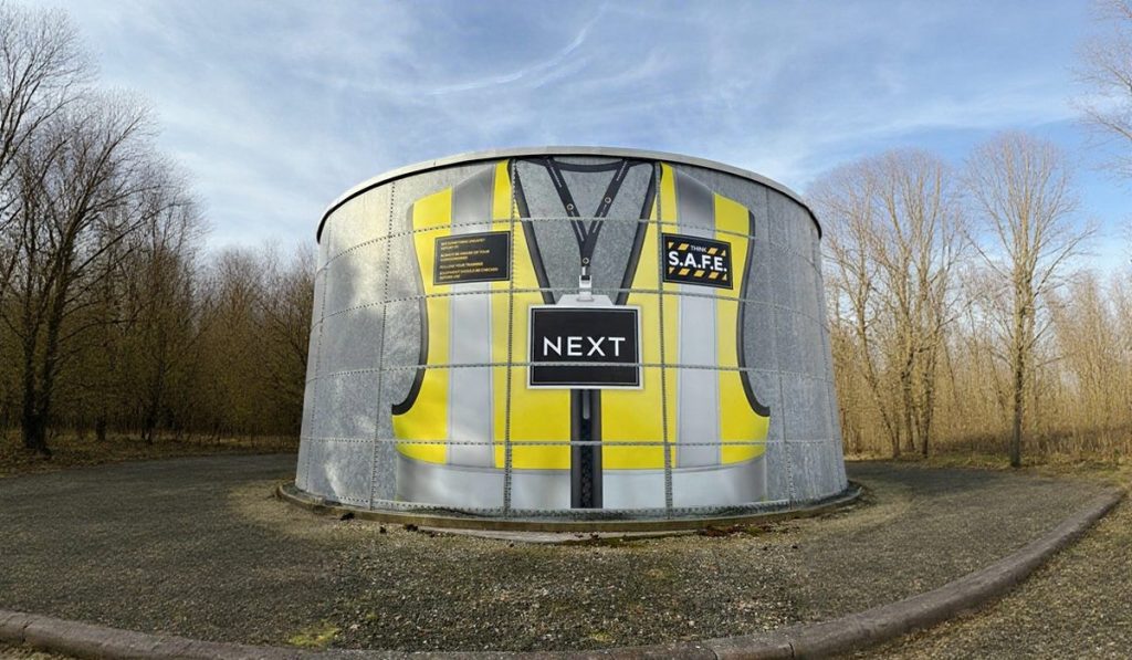 Circular metal structure painted to resemble a person’s high-visibility safety vest with yellow and gray panels and a central