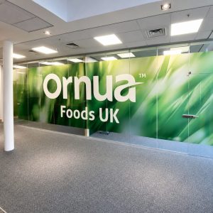 Office lobby with a large glass wall displaying 'Ornua Foods UK' in bold white letters on a green background