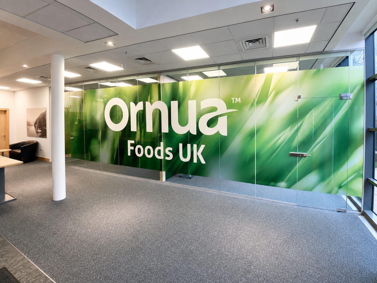 Office lobby with a large glass wall displaying 'Ornua Foods UK' in bold white letters on a green background