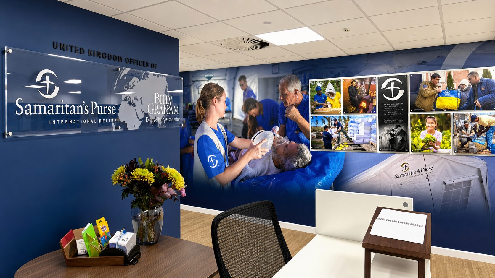 Reception area of a humanitarian charity office with blue wall signage: Samaritan's Purse and Billy Graham logos, plus a collage mural of relief images on the right panel.