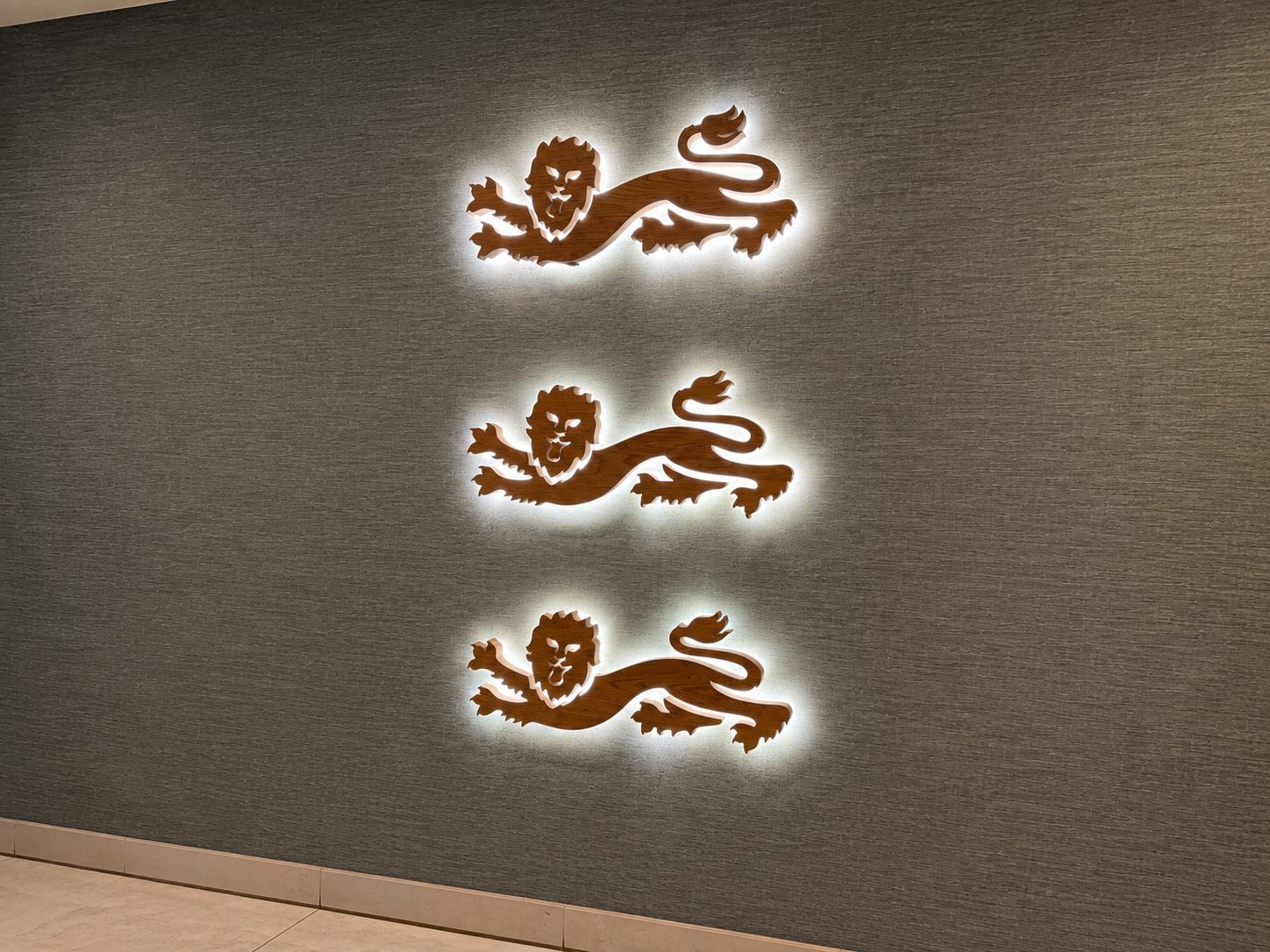 Three backlit brown lion silhouettes arranged vertically on a textured gray wall.