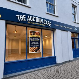 Front view of The Auction Café storefront with blue signage, street number 34, and a poster in the window.