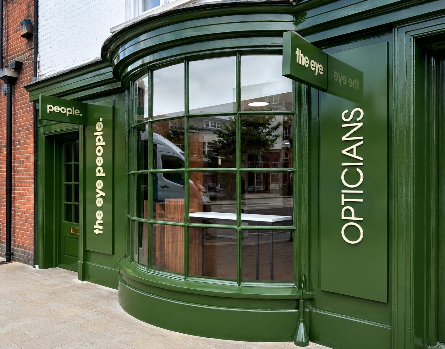 Green storefront of an eyewear shop with a large curved bay window, vertical white lettering, and signs reading 'the eye' and 'people' on the green facade.