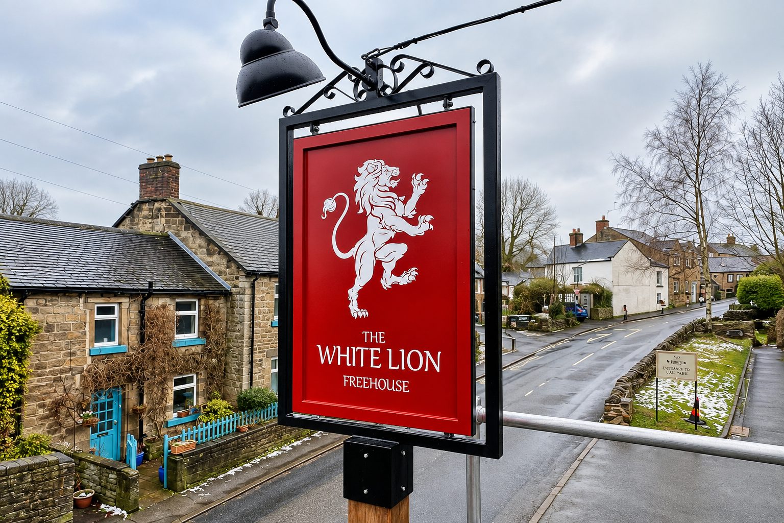 Red pub sign reading 'The White Lion Freehouse' with a white lion illustration, mounted over a street in a small village.