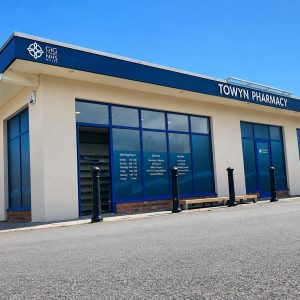 Towyn Pharmacy storefront with blue-framed windows on a sunny day.