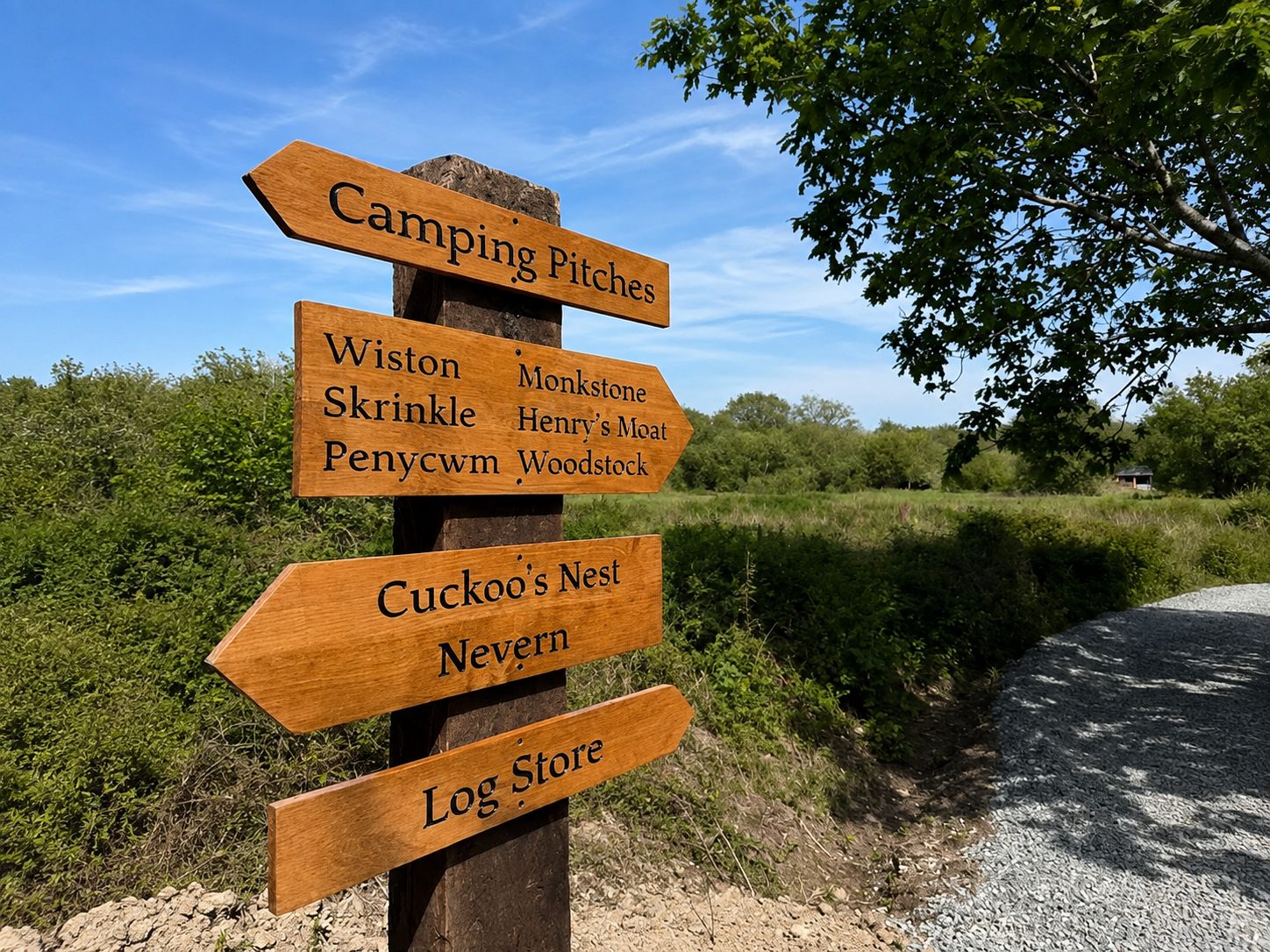 Wooden signpost with multiple directional arrows in a sunny park, pointing to Camping Pitches and nearby features.