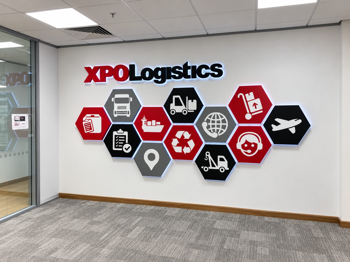Sign reading 'XPO Logistics' on a white wall with red/black hex icons representing logistics services in a hallway.