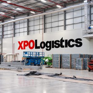 Warehouse interior with 'XPO Logistics' signage; pallets, forklift, and stacked materials ready for shipping.
