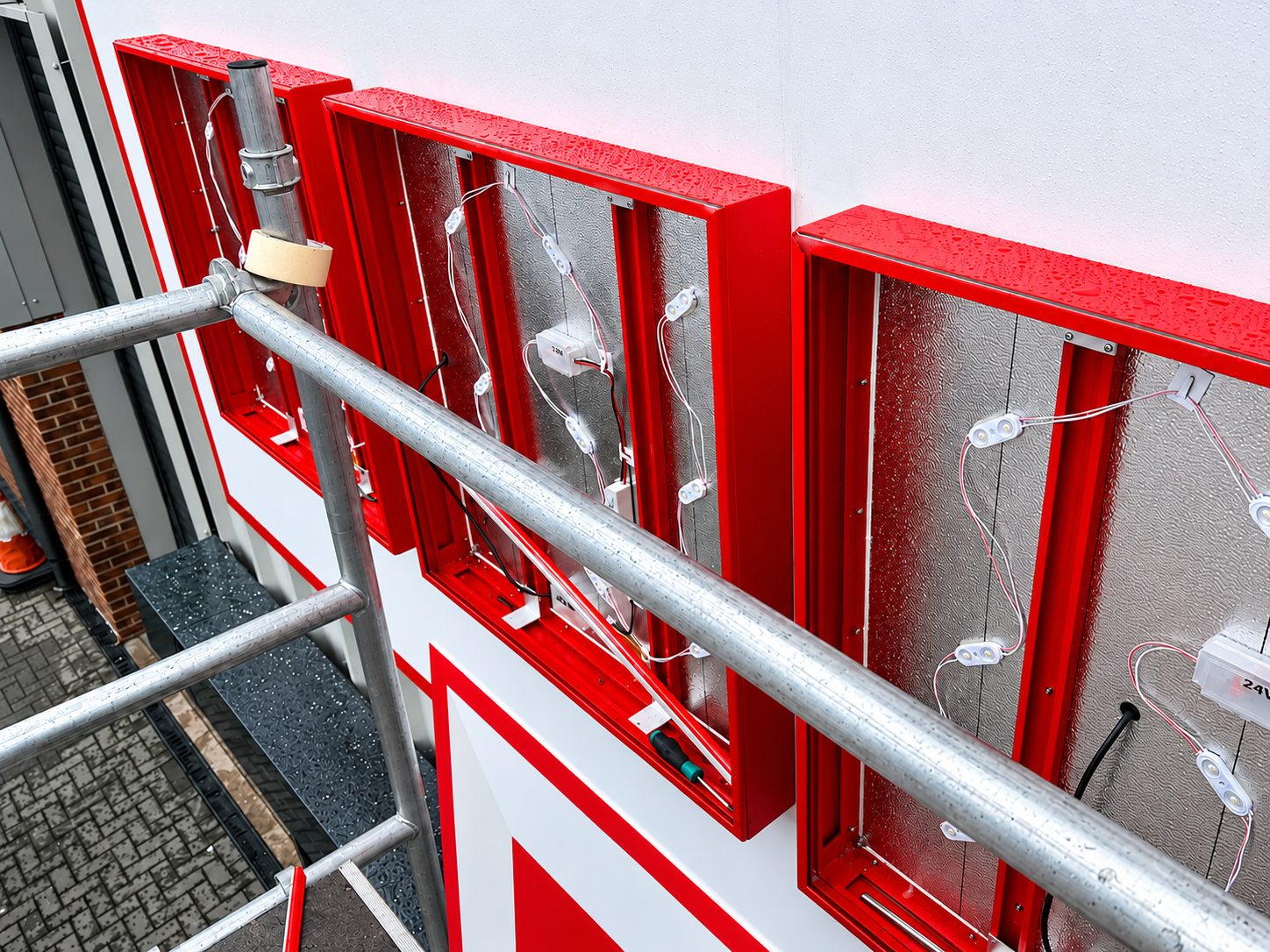 Exterior wall with bright red window frames and silver insulated panels, viewed from scaffolding during construction.