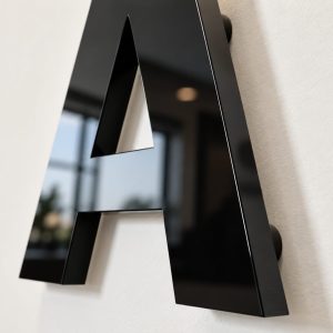 Close-up of a glossy black metal letter A mounted on a white wall in a modern office lobby.