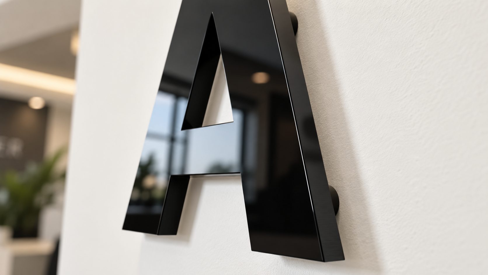 Close-up of a glossy black metal letter A mounted on a white wall in a modern office lobby.