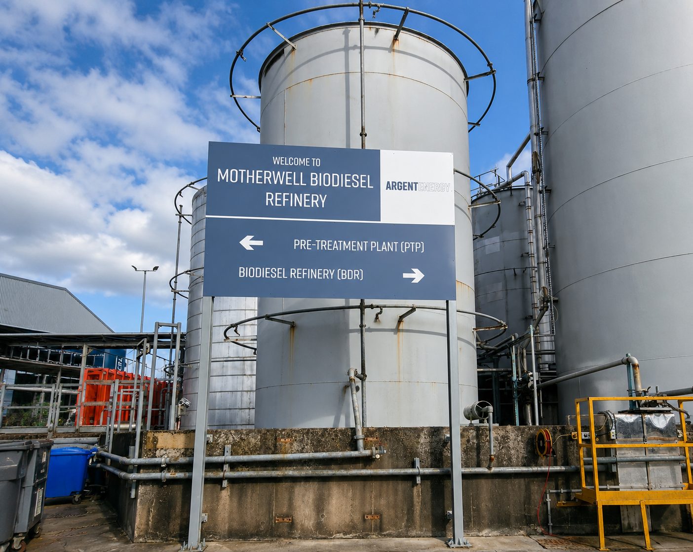Welcome sign at Motherwell Biodiesel Refinery directing to Pre-Treatment Plant on the left and Biodiesel Refinery on the right, with large metal tanks behind.